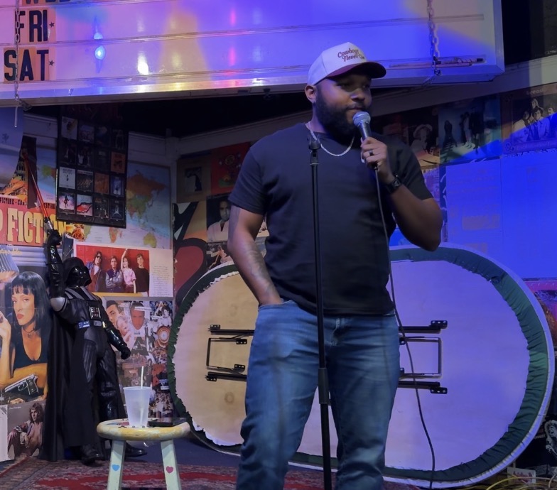 AJ Frazier speaking into a microphone during a comedy set